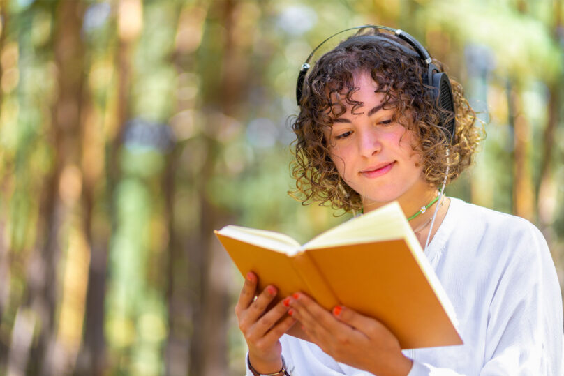nuori nainen ulkona lukee kirjaa kuulokkeet päässä coronaria kuntoutus psykoterapia
