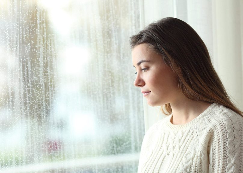 nuori nainen katsoo ulos sateisesta ikkunasta