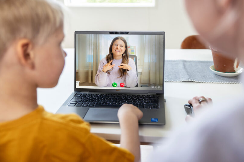 Poika ja äiti istuvat kotona kannettavan äärellä, jonka ruudussa näkyy puheterapeutti.