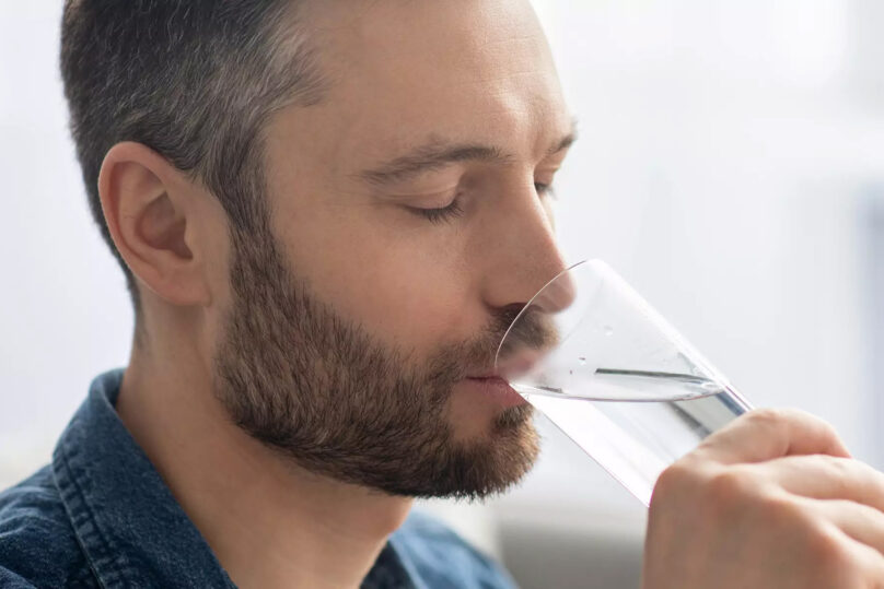 Tummahiuksinen mies juo vettä lasista.