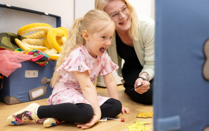 Vaaleahiuksinen tyttö ja puheterapeutti tekevät peilin edessä äänneharjoitusta.