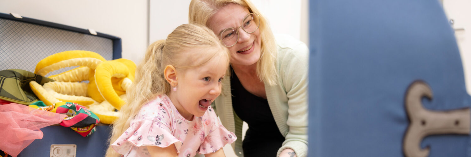 Vaaleahiuksinen tyttö ja puheterapeutti tekevät peilin edessä äänneharjoitusta.