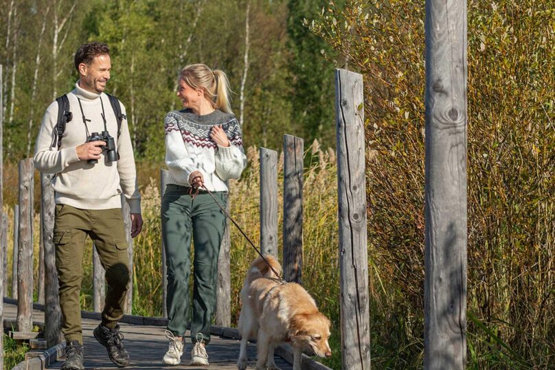 Mies ja nainen kävelemässä pitkospuilla, taluttaen koiraa virkeän ja hyvin nukkuneen näköisinä.