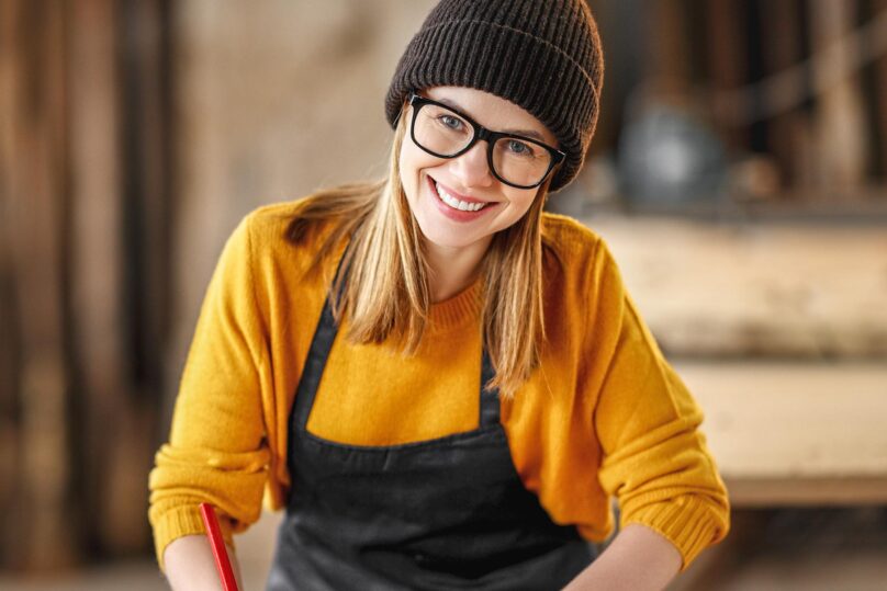 nuori nainen hymyilee kameraan pipo ja silmalasit paassa