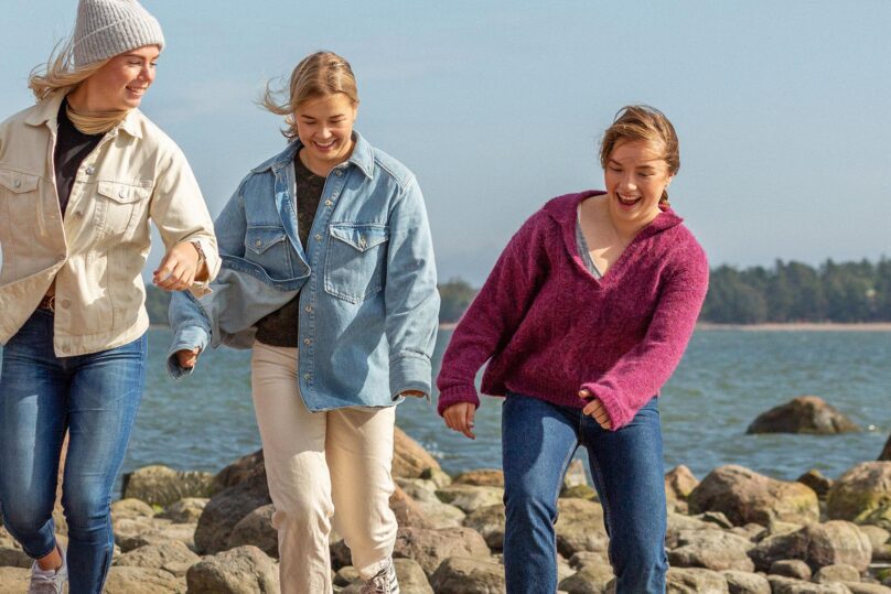 kolme nuorta naista kavelevat rannalla ja hymyilevat