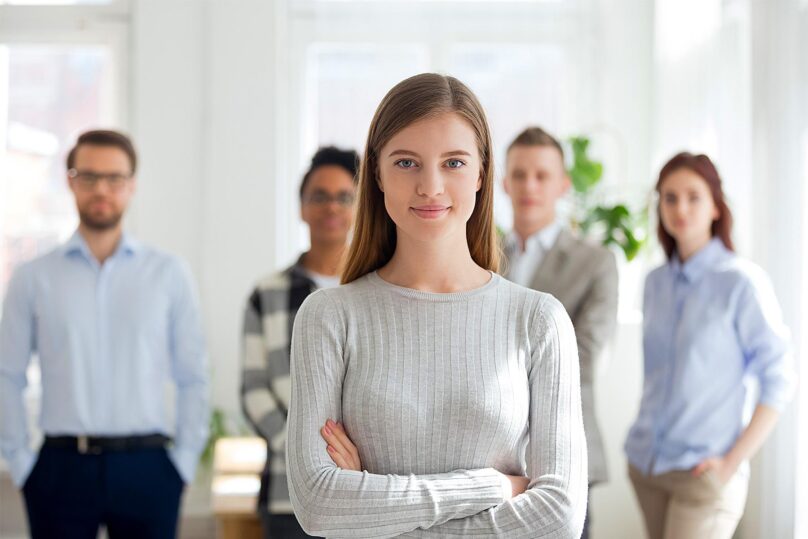 nuori nainen etualalla ja toimiston tyontekijoita taustalla rivissa