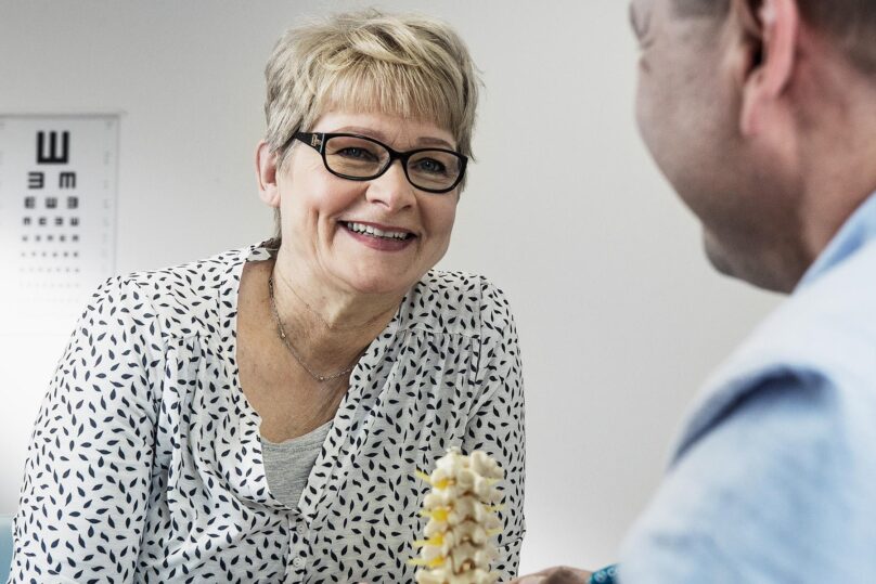 Naisasiakas hymyilee mieslääkärille vastaanotolla.