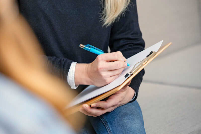 Lähikuva naisen käsistä kirjoittamassa muistiinpanoja lehtiöön.