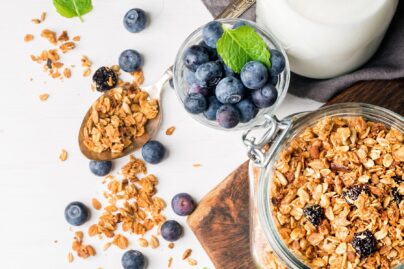 Pöydällä aseteltuna aamiaistarpeita; mysliä, maitoa ja mustikoita.