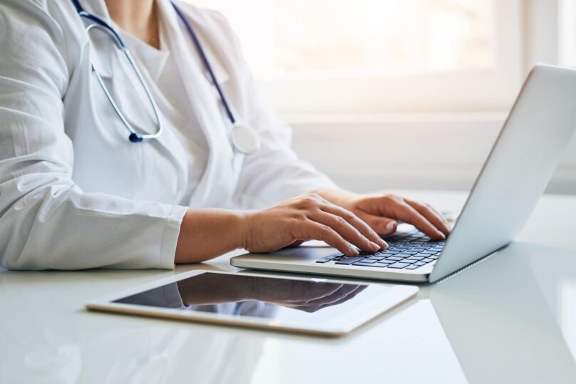 Lähikuva naislääkärin käsistä kirjoittamassa kannettavalla tietokoneella.
