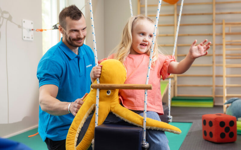 Coronaria kuntoutuspalvelut toimintaterapian lapsiasiakas on pitkässä keinussa pehmolelun kanssa.
