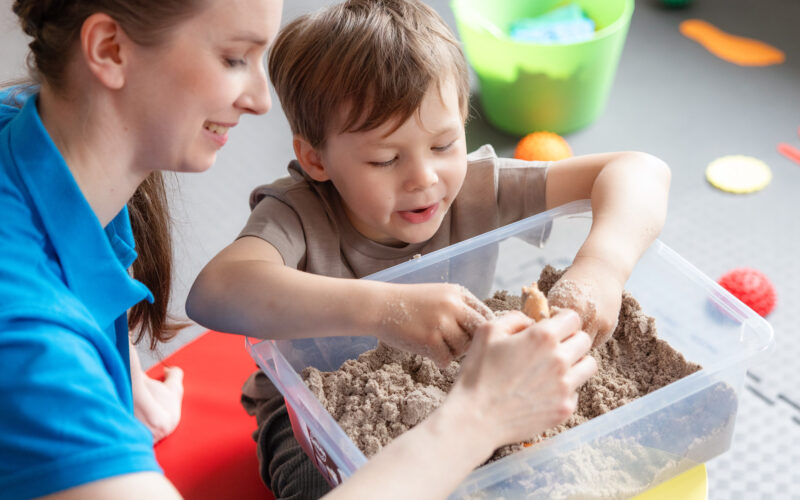Coronaria kuntoutuspalvelut toimintaterapian lapsiasiakas etsii terapeutin kanssa hiekasta esineitä.