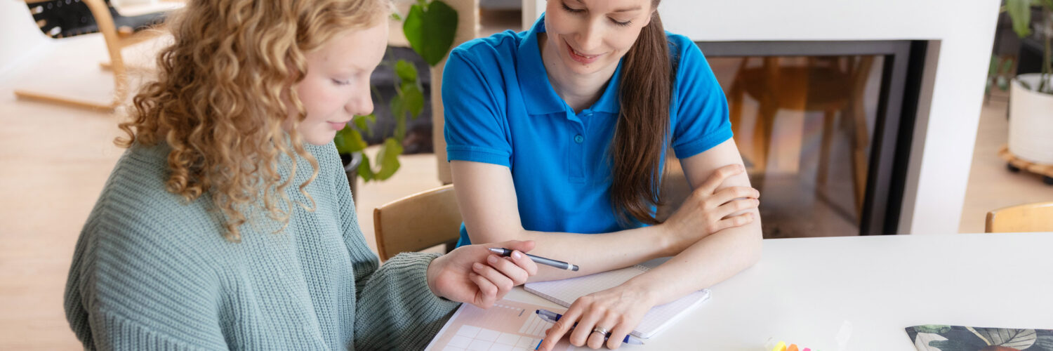 Coronaria kuntoutuspalvelut toimintaterapian nuori asiakas tekee terapeutin kanssa suunnitelmaa keittiönpöydän ääressä.