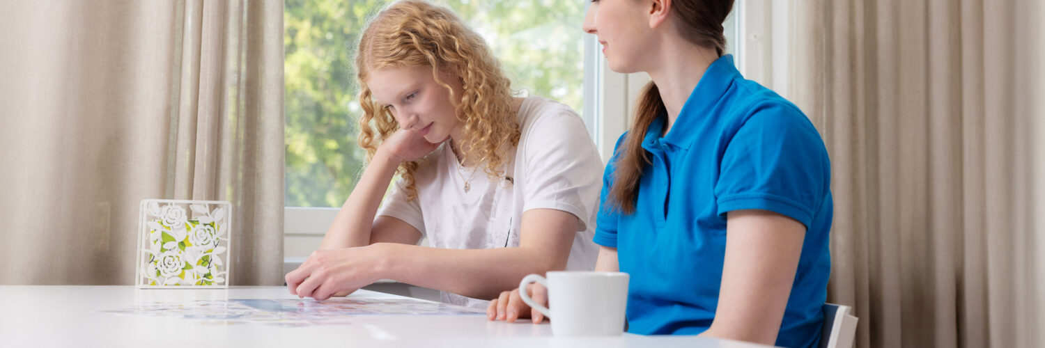 Coronaria kuntoutuspalvelut psykiatrinen toimintaterapia, teinityttö tekee terapeutin kanssa pöydän ääressä tehtävää.