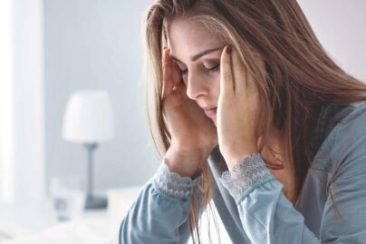 Unettomuudesta kärsivä henkilö istuu sängyllä väsyneenä.