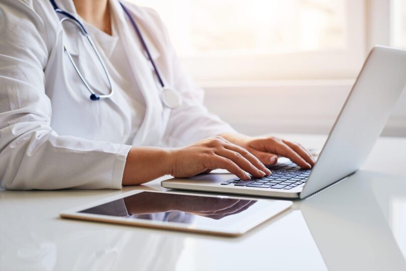 Naislääkäri kirjoittaa kannettavan tietokoneen näppäimistöllä lähikuvassa.