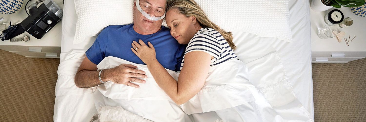 Varttunut pariskunta nukkumassa sängyssä ja miehellä on CPAP-laite.