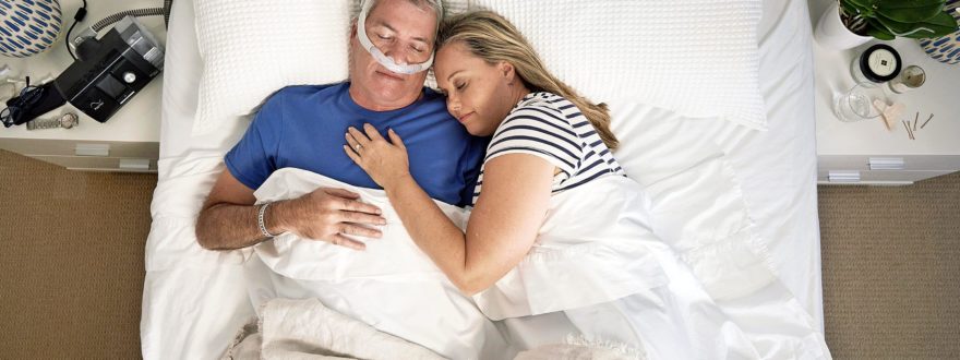 Varttunut pariskunta nukkumassa sängyssä ja miehellä on CPAP-laite.