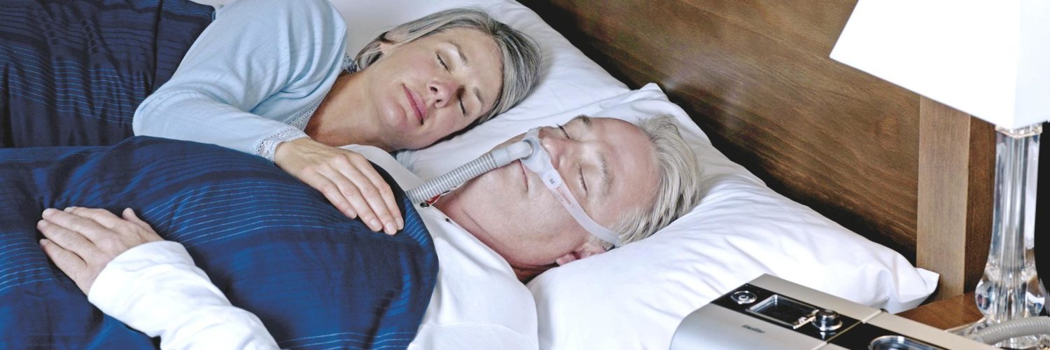 Iäkäs pariskunta nukkuu sängyssä ja miehellä on CPAP-laitteet.