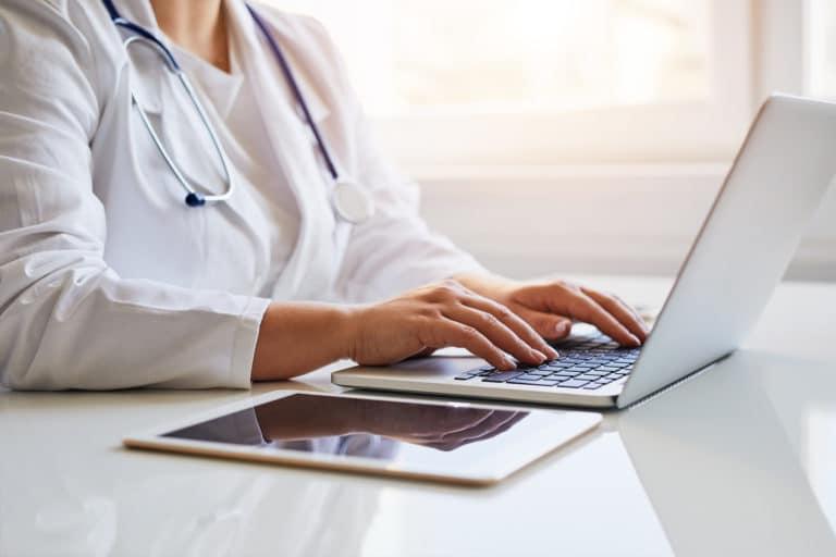 Naislääkäri istuu ja kirjoittaa tietokoneellaan.