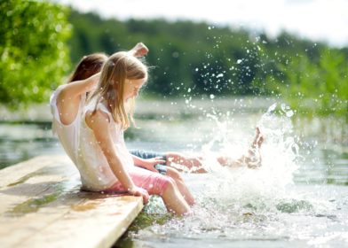 Kaksi tyttöä istuu laiturilla ja kastavat jalkojaan veteen.