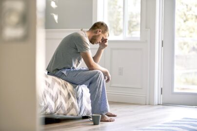 Mies istuu yöpuku päällä pöydän laidalla ja pitelee käsillään päätään.