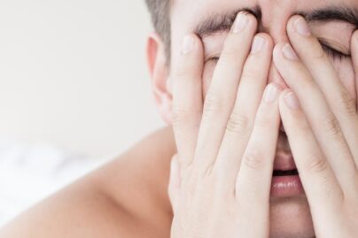 Väsynyt nuori mies pitää käsiä kasvoillaan lähikuvassa.