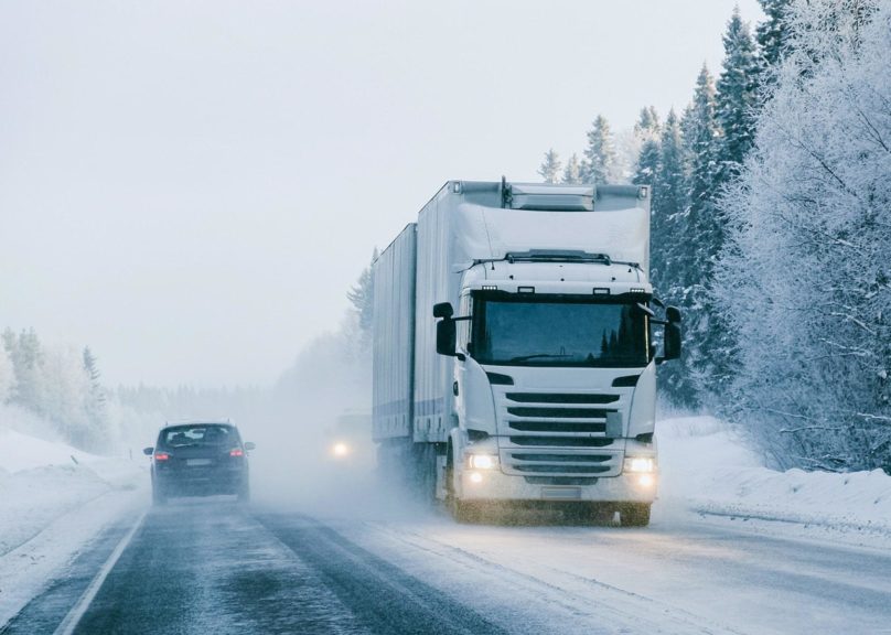 Valkoinen rekka-auto ajaa Lapissa lumisella tiellä talvella.