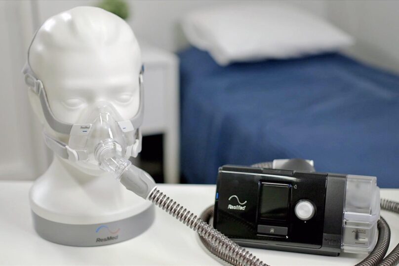 Resmedin CPAP-laite pöydällä ja maski nuken päässä.