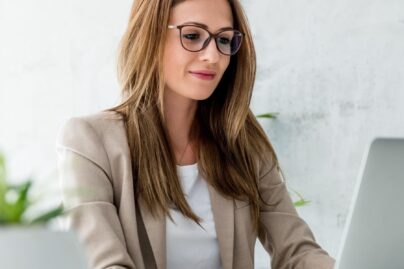 FAQ Ruskeahiuksinen nainen istuu konttorilla tietokoneen ääressä.