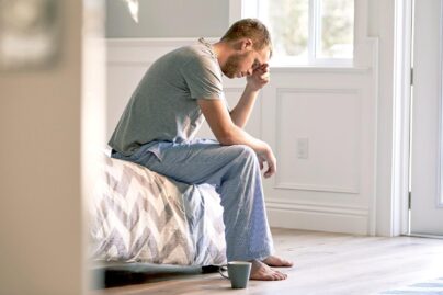 väsynyt mies nojaa käteensä sängyn reunalla