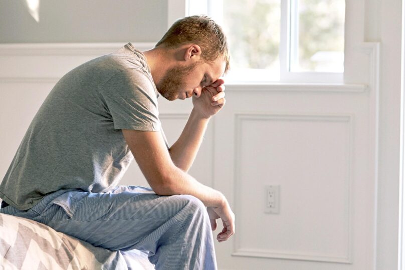 väsynyt mies nojaa käteensä sängyn reunalla