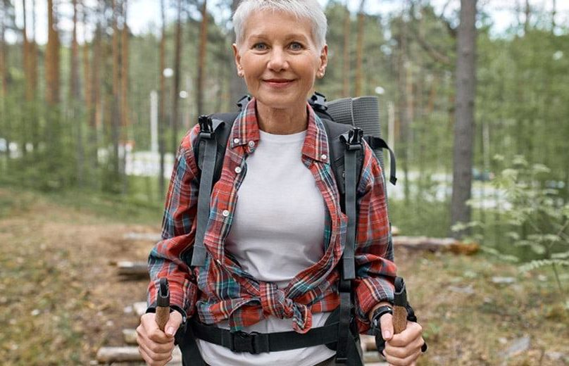 keski-ikäinen valkohiuksinen nainen sauvakävelee metsässä