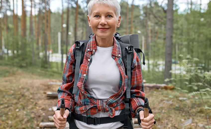 keski-ikäinen valkohiuksinen nainen sauvakävelee metsässä