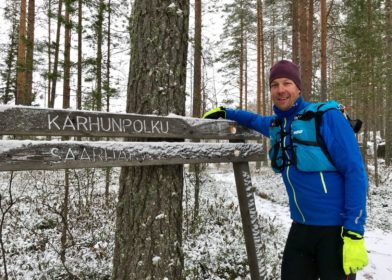 Posio liikkuu -hyvinvointikampanjan suojelija Mikko Peltola nojaa kylttiin metsässä.