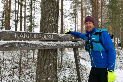 Posio liikkuu -hyvinvointikampanjan suojelija Mikko Peltola nojaa kylttiin metsässä.