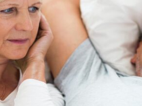 Iäkkäämpi pariskunta, jossa mies kuorsaa ja nainen pitää sormia korvissa.