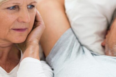 Iäkkäämpi pariskunta, jossa mies kuorsaa ja nainen pitää sormia korvissa.