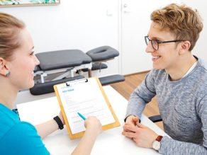 Coronaria Kuntoutuksen fysioterapeutti täyttämässä lomaketta miespuolisen asiakkaan kanssa pöydän ääressä.