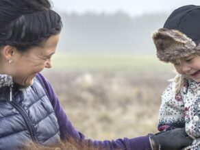 Äiti naurattaa tyttöä hevosen selässä.