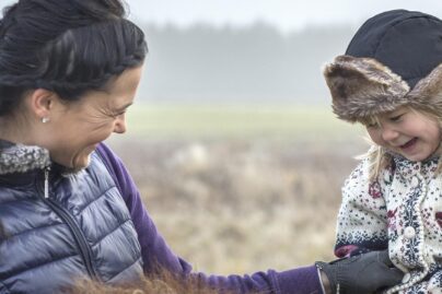 Äiti naurattaa tyttöä hevosen selässä.