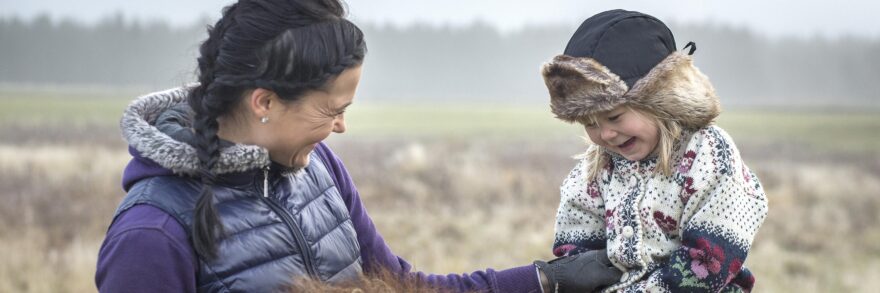 Äiti naurattaa tyttöä hevosen selässä.