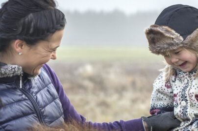 Äiti naurattaa tyttöä hevosen selässä.