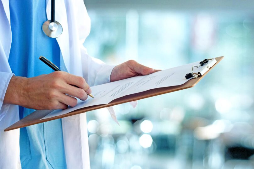 Mieslääkäri kirjoittaa potilastietoja, lähikuva käsistä.