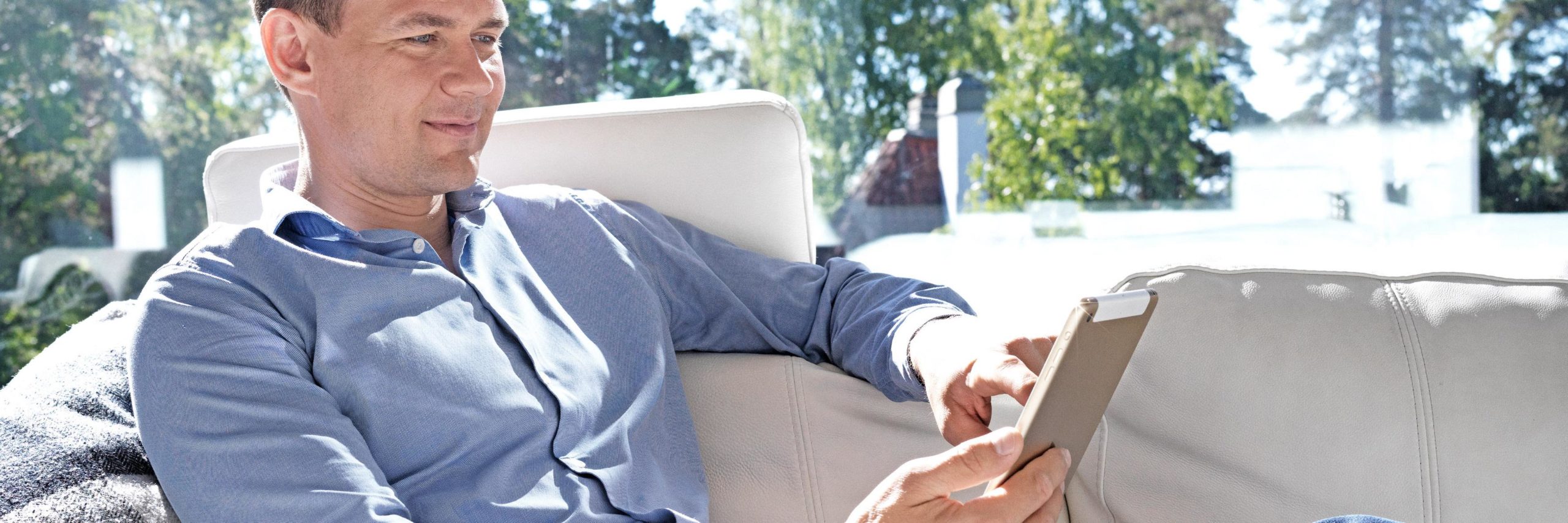 Coronarian erikoissairaanhoidon mieslääkäri istuu sohvalla iPad kädessä.