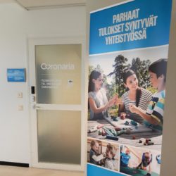 Coronaria kuntoutus-ja terapiapalvelut Raaseporin Sisäänkäynnin ovesta kuva, jonka vieressä Coronarian mainos roll-up.