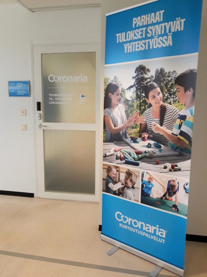 Coronaria kuntoutus-ja terapiapalvelut Raaseporin Sisäänkäynnin ovesta kuva, jonka vieressä Coronarian mainos roll-up.