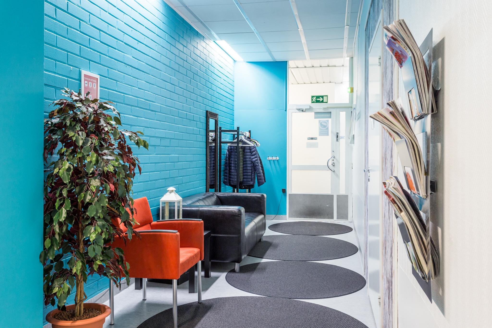 Coronaria kuntoutus- ja terapiapalvelut Oulun toimipisteen sisääntulokäytävä, jossa turkoosi seinä, tuoli ja sohva odotusta varten.