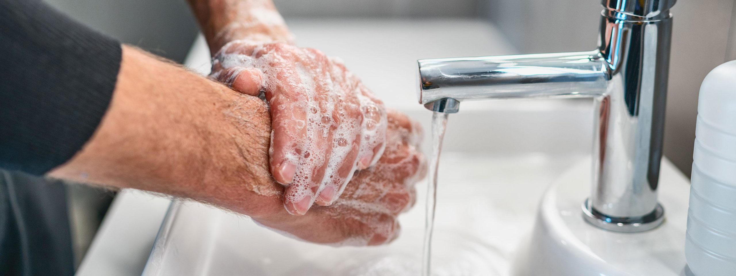 Mies pesee käsiä vesihanan alla
