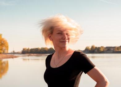 Nainen heiluttaa hiuksia rannalla, jonne paistaa aurinko